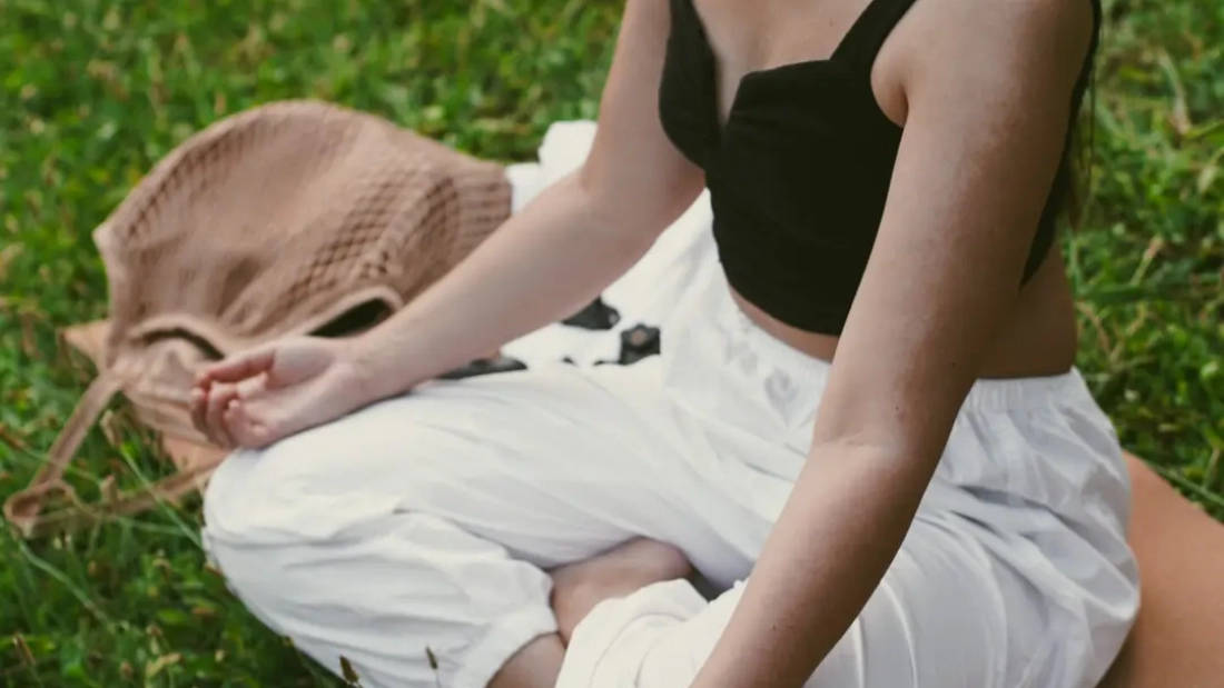 Corgi dog lying on grass in park next to girl sitting on yoga mat meditating. Soft focus
